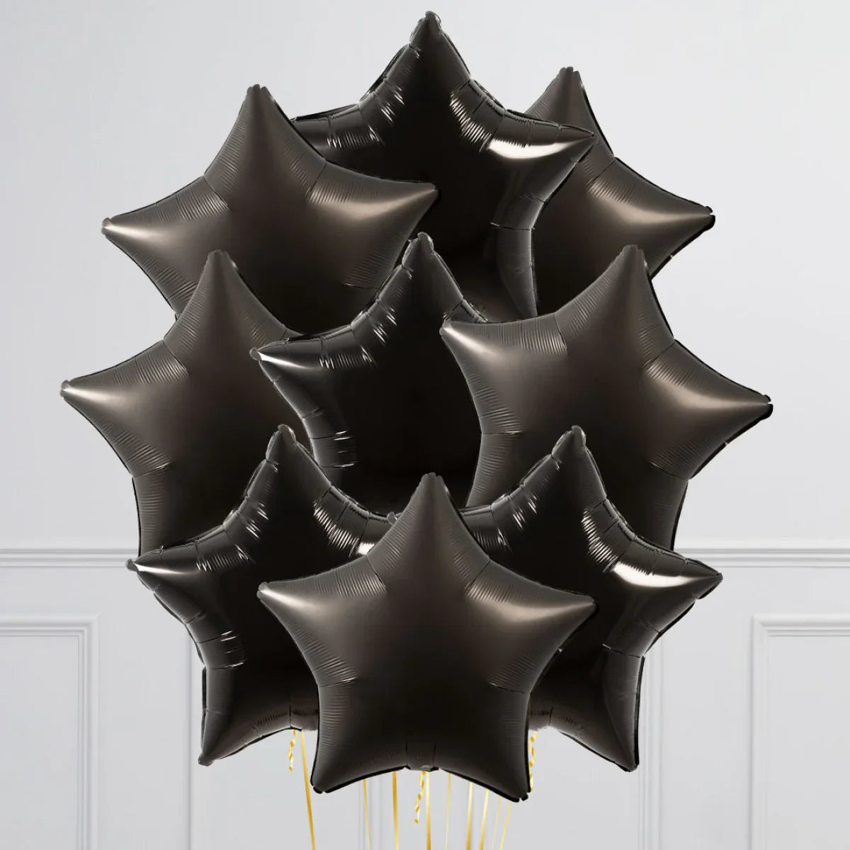 Cluster of shiny black star-shaped foil balloons against a plain light wall background