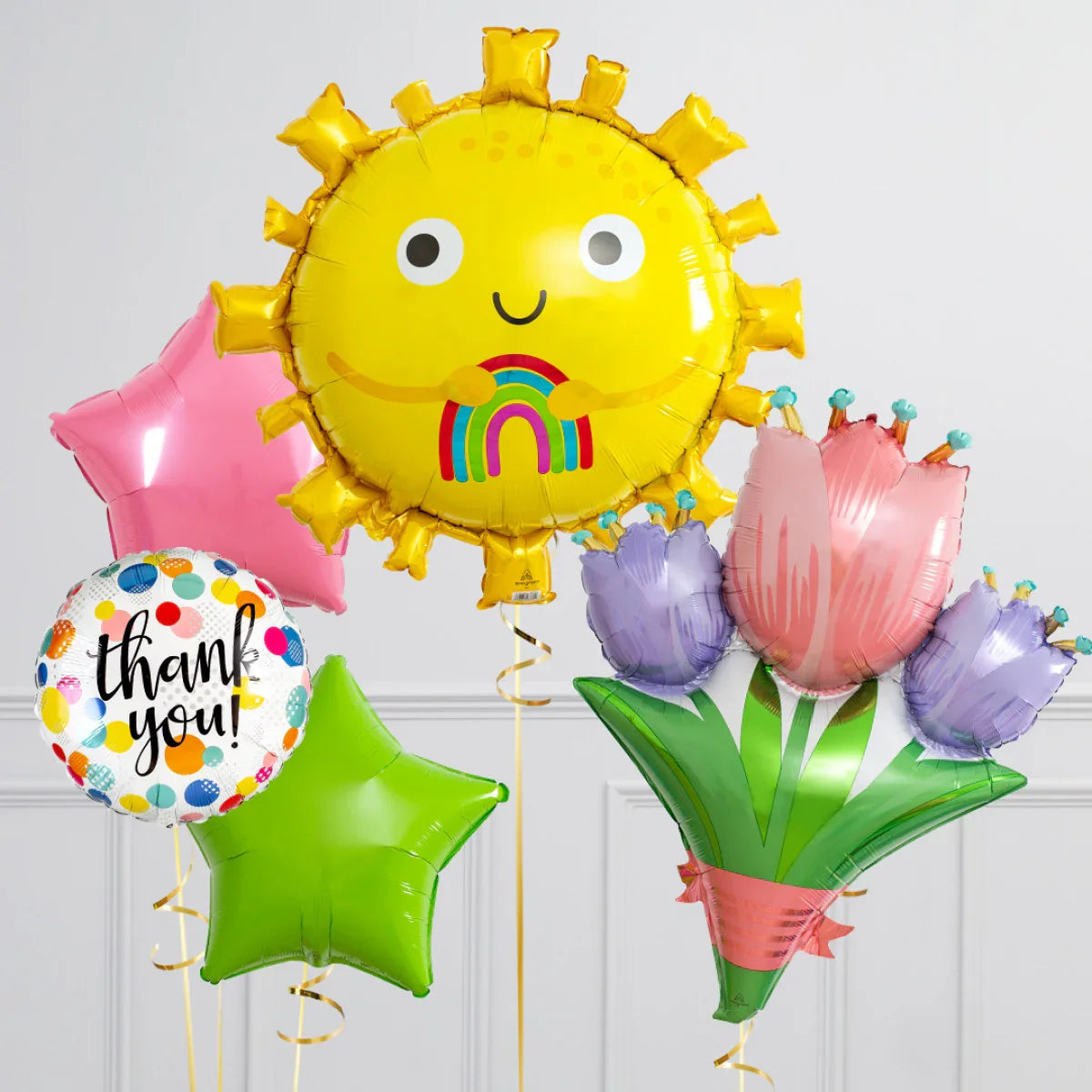 Colorful helium balloons including a smiling sun holding a rainbow, thank you, stars, and bouquet shapes
