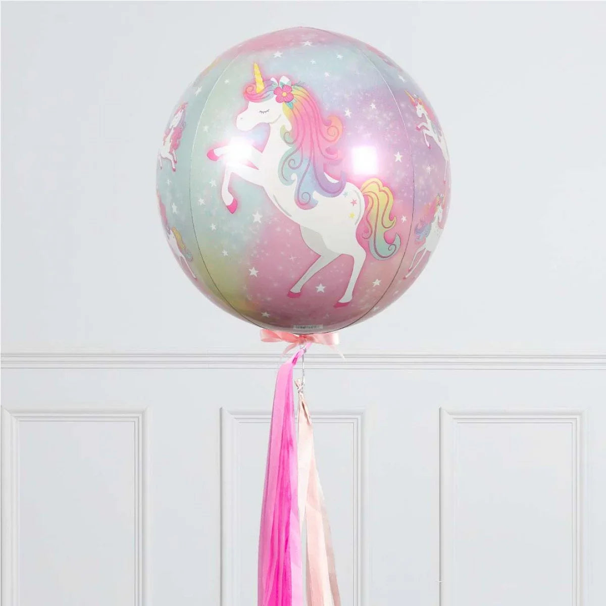 Round pastel unicorn balloon with pink and purple ribbons against white paneled wall